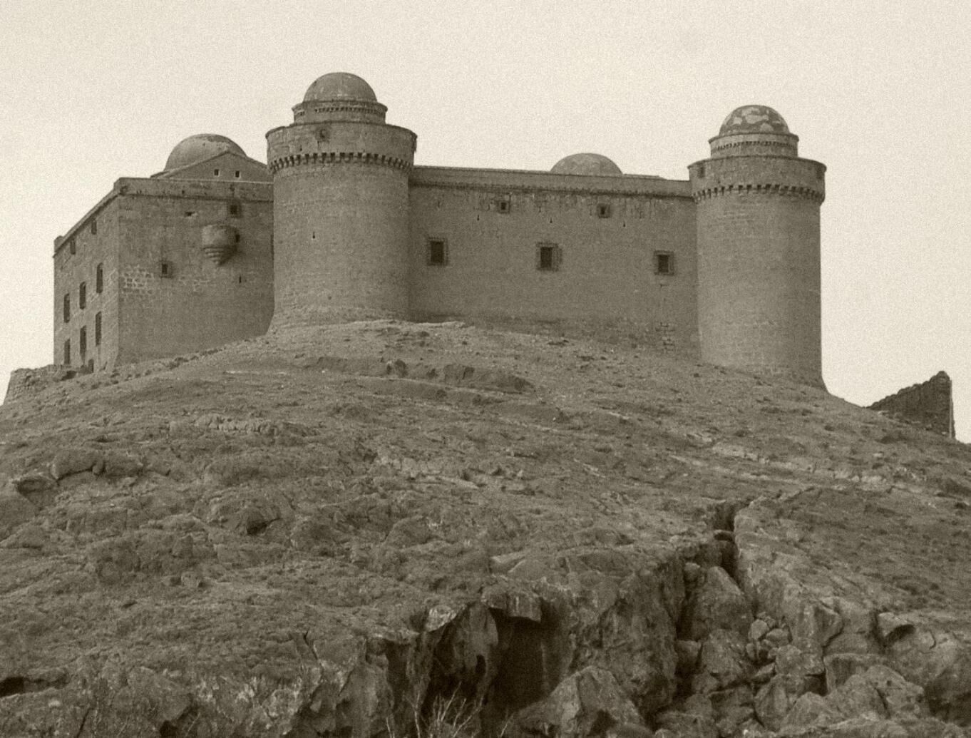 Eine große, historische Burg mit mehreren Türmen und einer befestigten Mauer, gelegen auf einem felsigen Hügel.