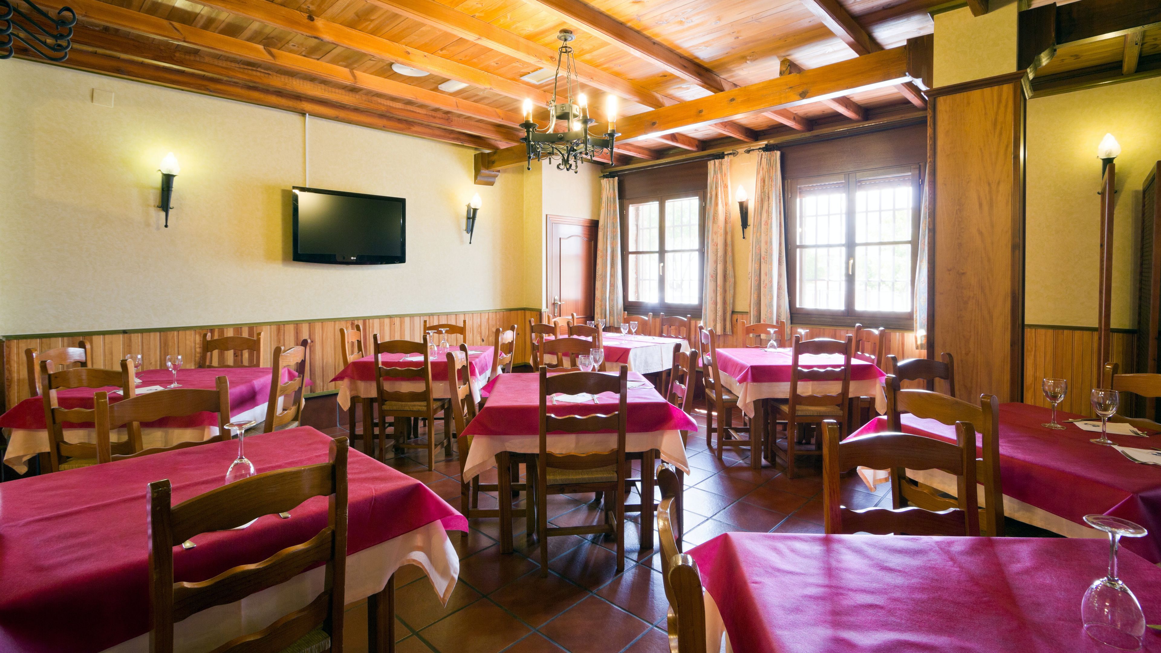 Un restaurante con mesas y sillas de madera, un candelabro y un televisor de pantalla plana en la pared.