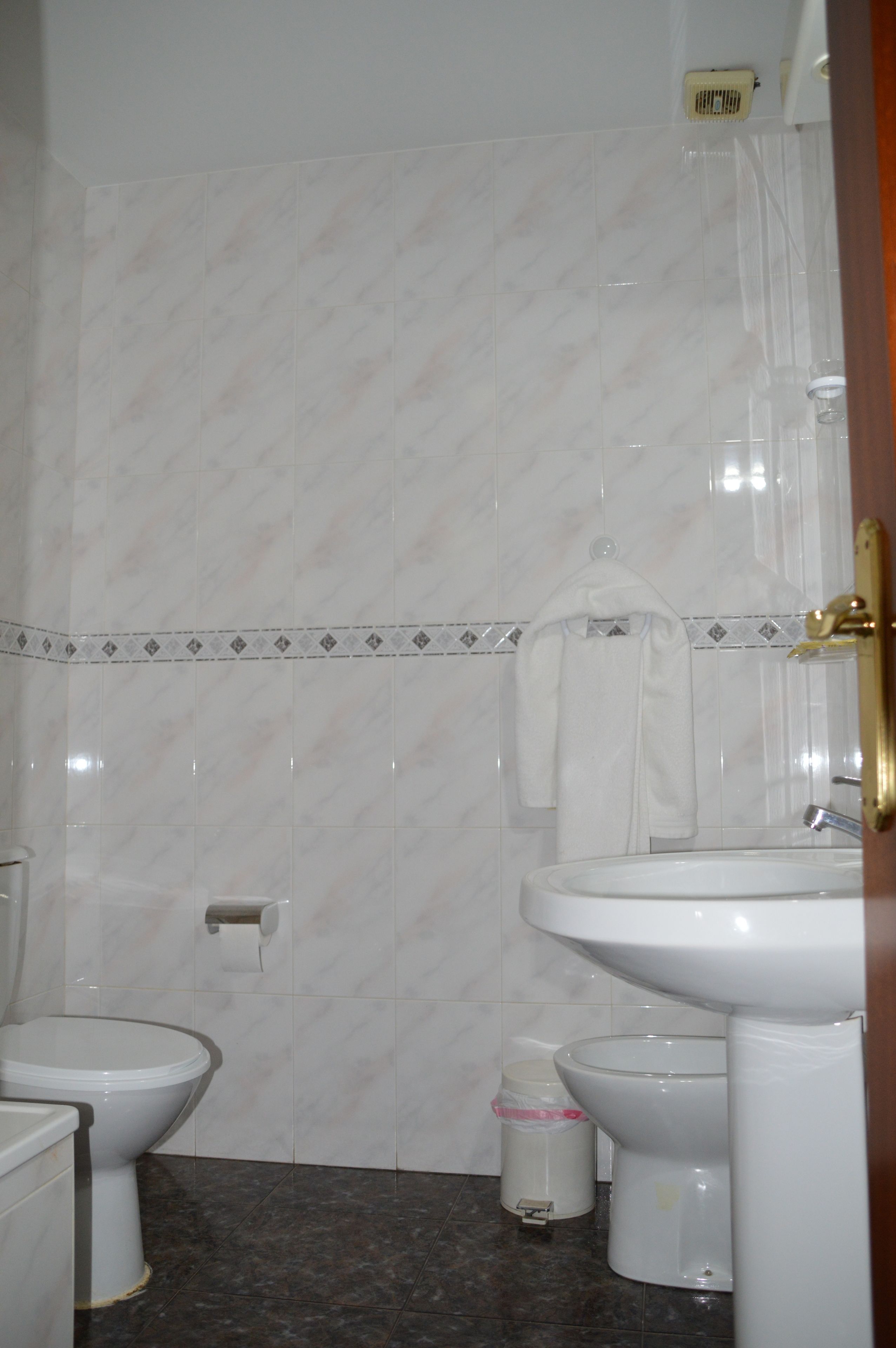 A bathroom with two toilets, a sink, a trash bin, and a towel hanging on the wall.