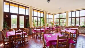 A restaurant with multiple tables covered with pink tablecloths, wooden chairs, and potted plants.