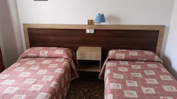 Una habitación con dos camas individuales, una mesita de noche, una lámpara y un pequeño armario de madera.