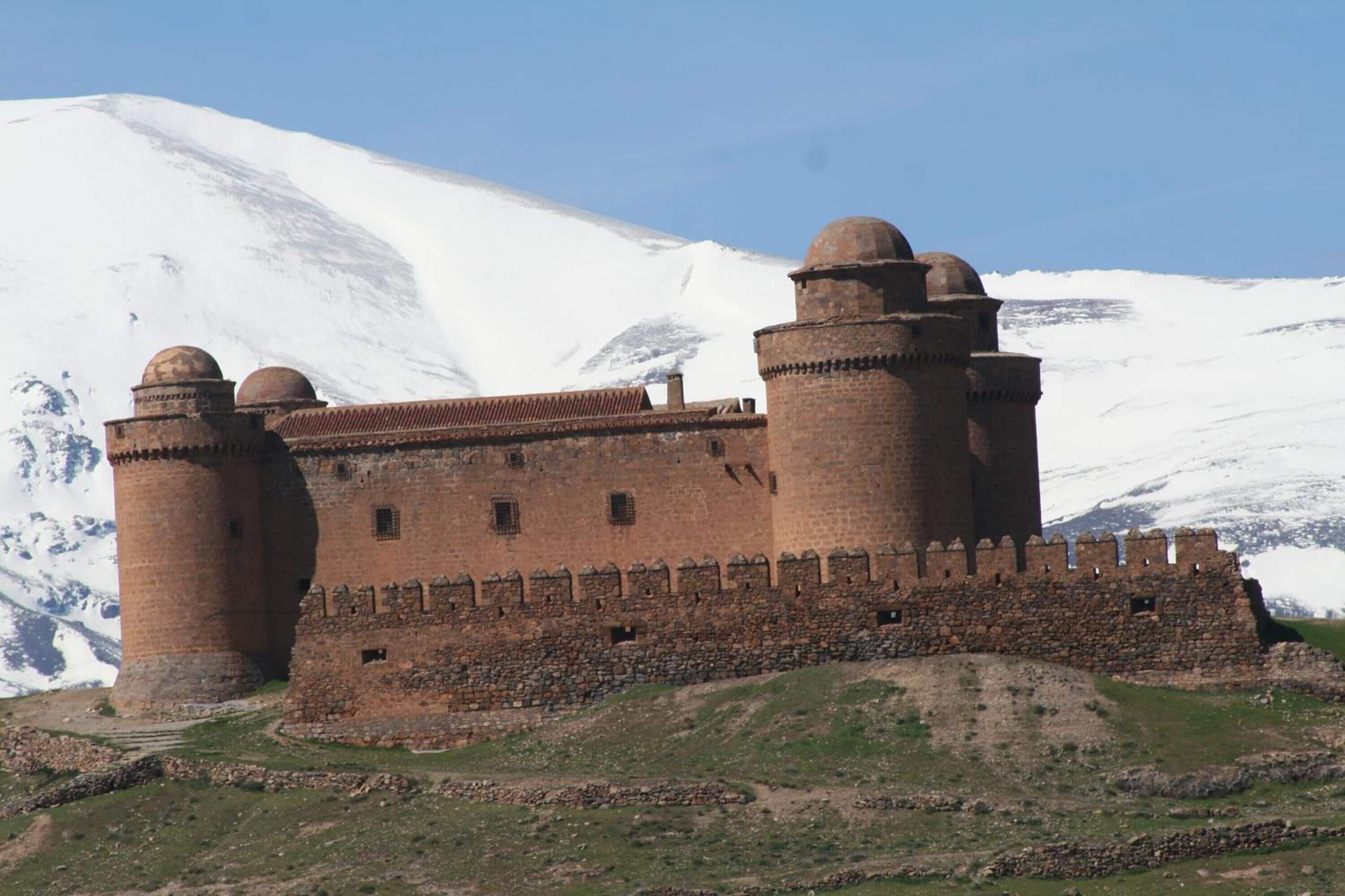 Een historisch stenen kasteel met twee opvallende torens, omgeven door een besneeuwd landschap.