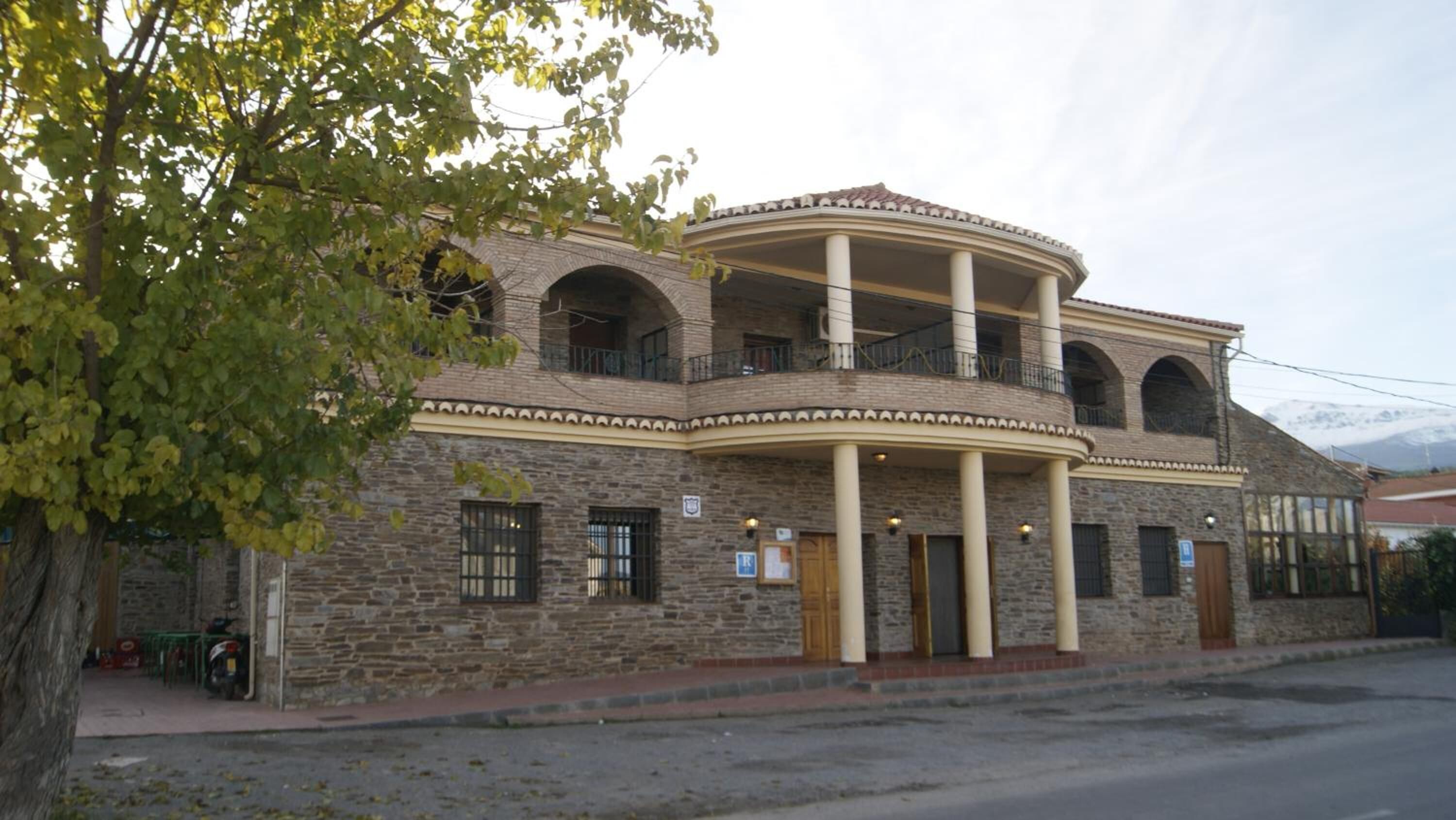 Ein zweistöckiges Steinhaus mit einem gebogenen Balkon, mehreren Fenstern und einem kleinen Eingang.