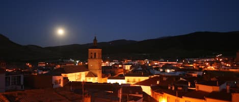 A town at night with a prominent clock tower, illuminated buildings, and a clear view of the moon.