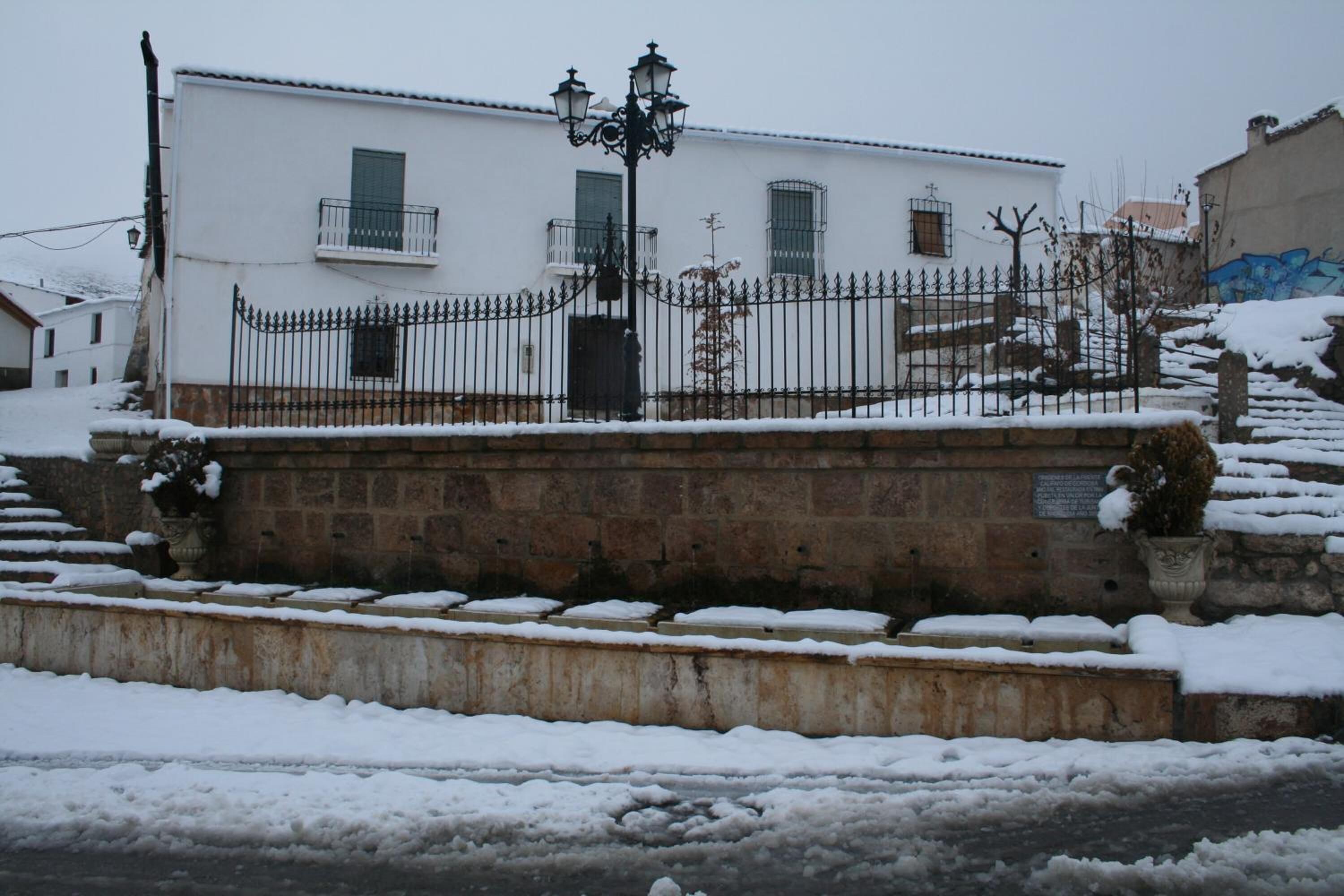 Un edificio blanco con balcón, pared de piedra y cerca de metal.