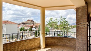 A balcony with a view of a historic hilltop fortress, a paved area, and a brick wall.
