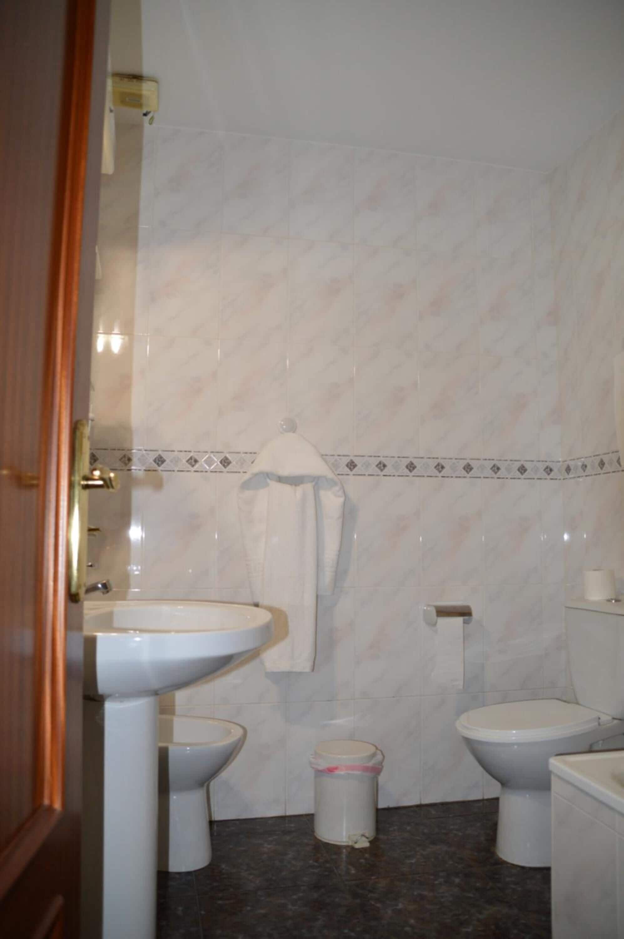 Une salle de bain avec un lavabo, deux toilettes, une poubelle et une serviette accrochée au mur.