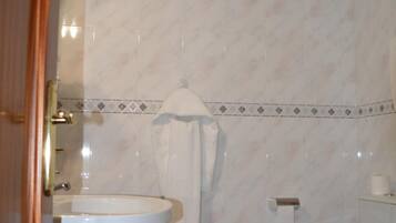 Une salle de bain avec un lavabo, deux toilettes, une poubelle et une serviette accrochée au mur.