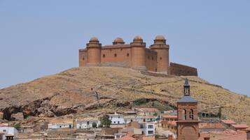 Una fortaleza histórica en una colina con un campanario, rodeada por un pueblo con edificios de techos de teja.