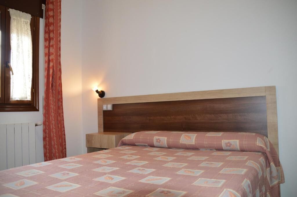 A bedroom with a wooden headboard, a bed with a patterned bedspread, a bedside table, and a wall-mounted light.