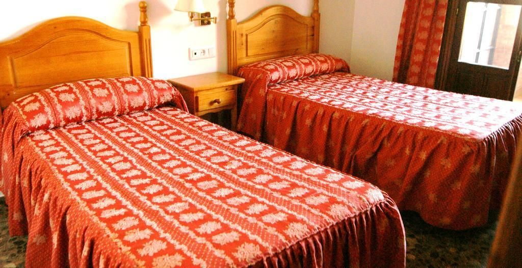 A room with two beds, each with a patterned bedspread, a wooden headboard, a nightstand, and a lamp.