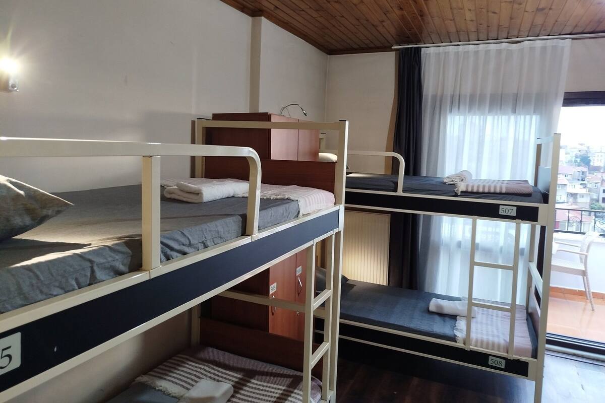 Een slaapzaal met stapelbedden, houten plafond en een raam met gordijnen.