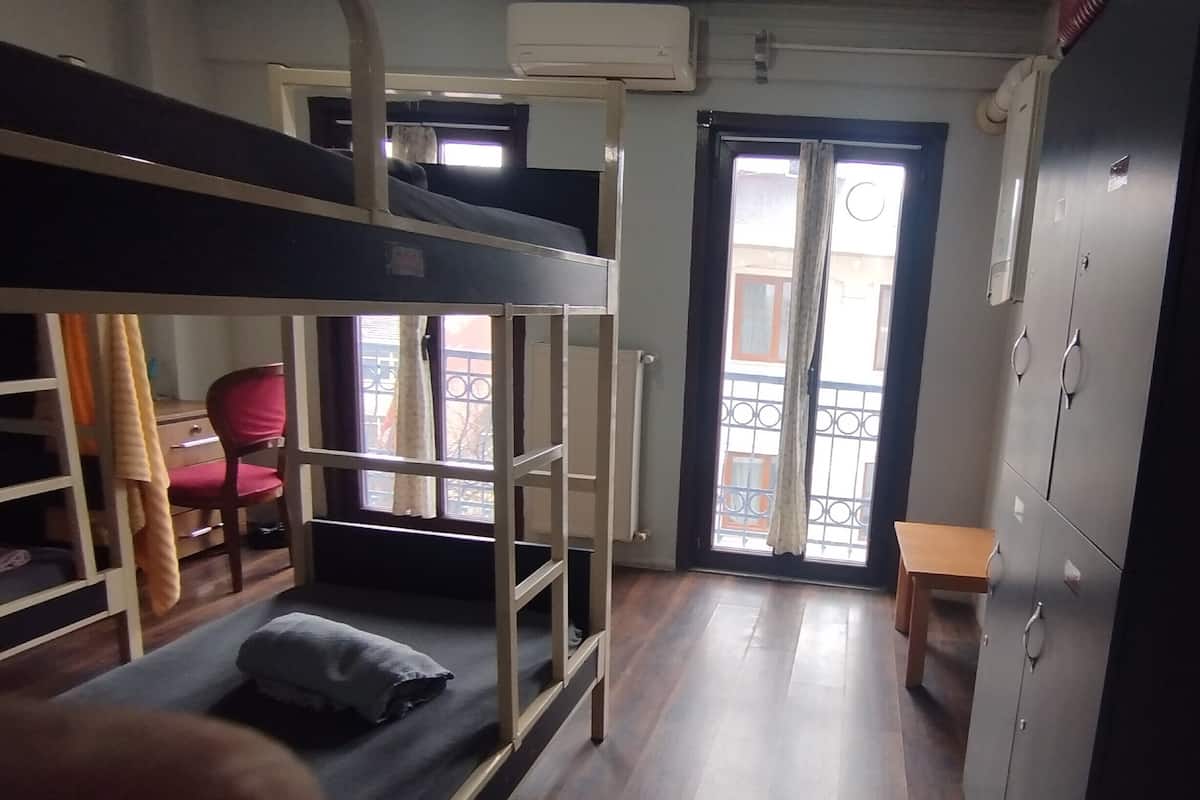 A dormitory room with bunk beds, a desk, a chair, and a wardrobe.