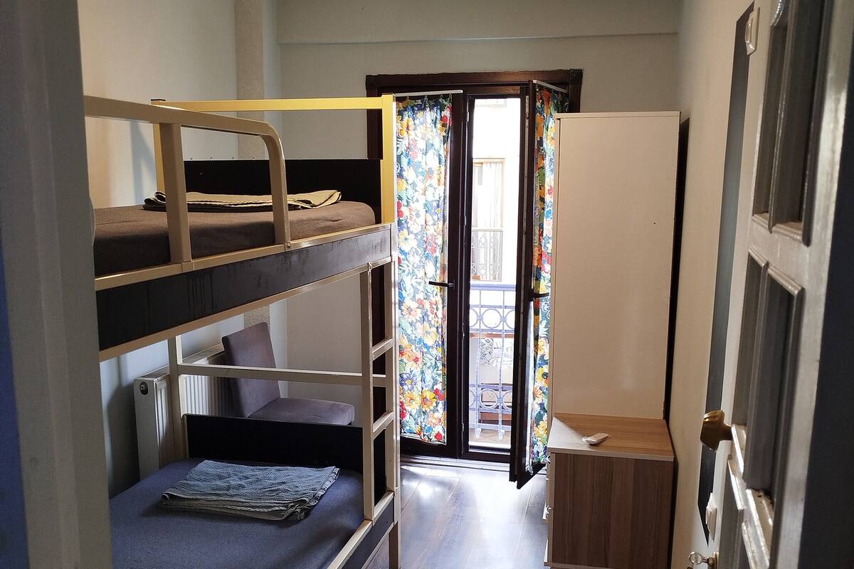 Een kamer met stapelbedden, een houten bureau en een deur naar een balkon.