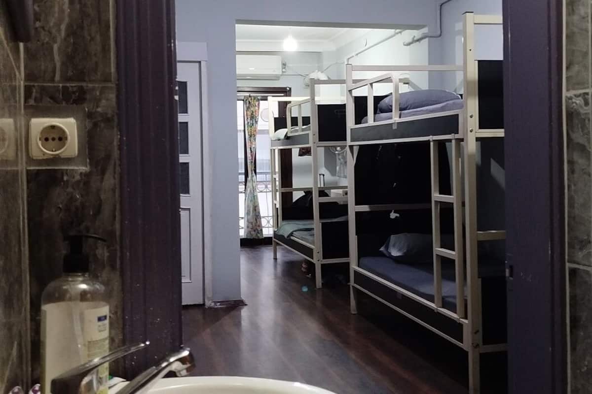 A bathroom with a sink, mirror, and bunk beds in the background.