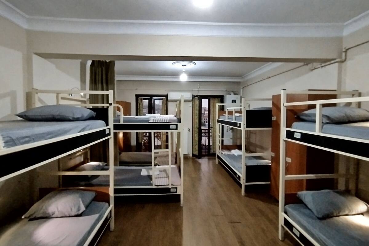 Een slaapzaal met stapelbedden gerangschikt in een U-vorm, een deur naar een balkon en een plafondlamp.
