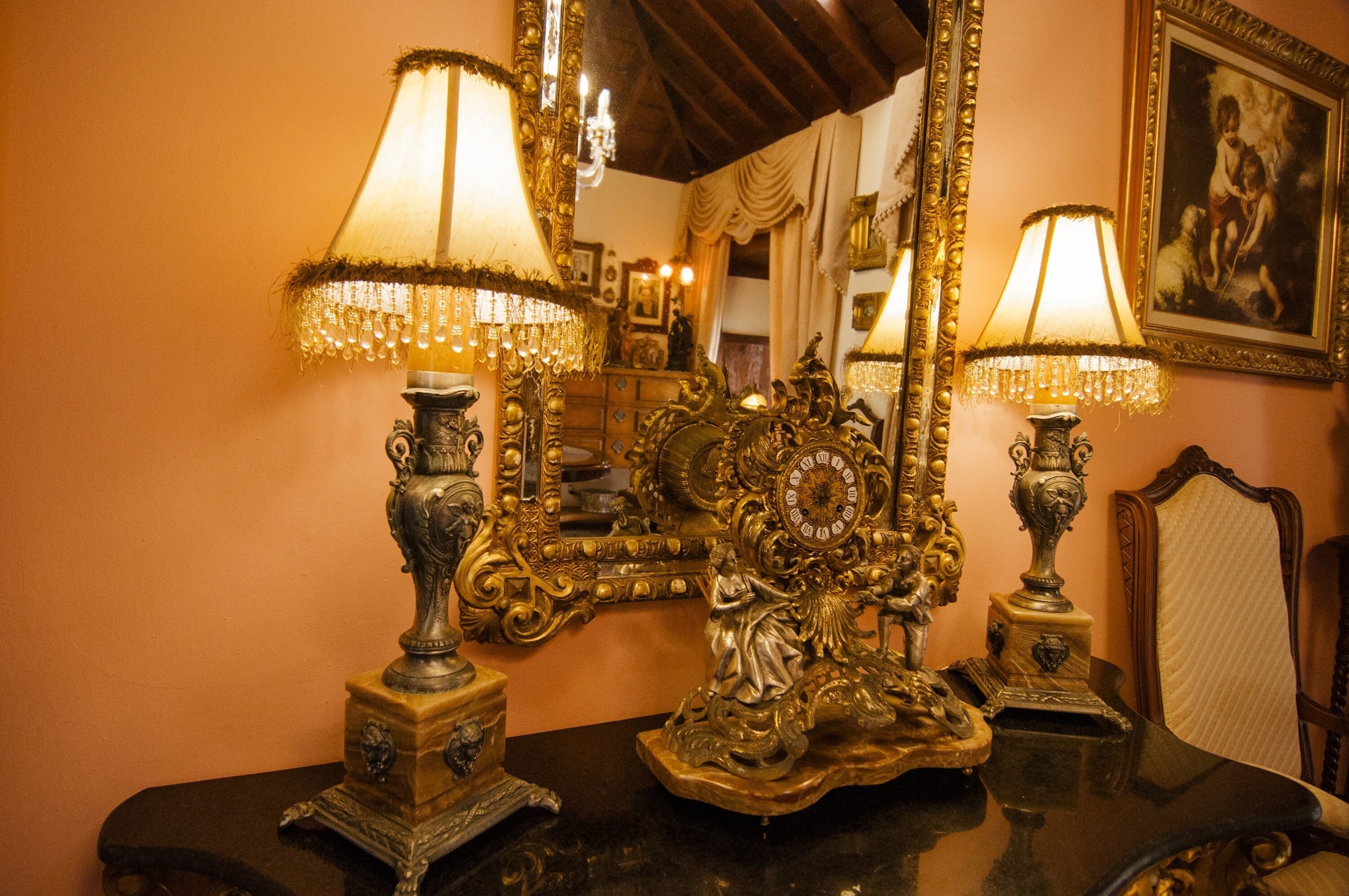 Una habitación con muebles antiguos y ornamentados, incluyendo un espejo grande y dos lámparas de diseños elaborados.