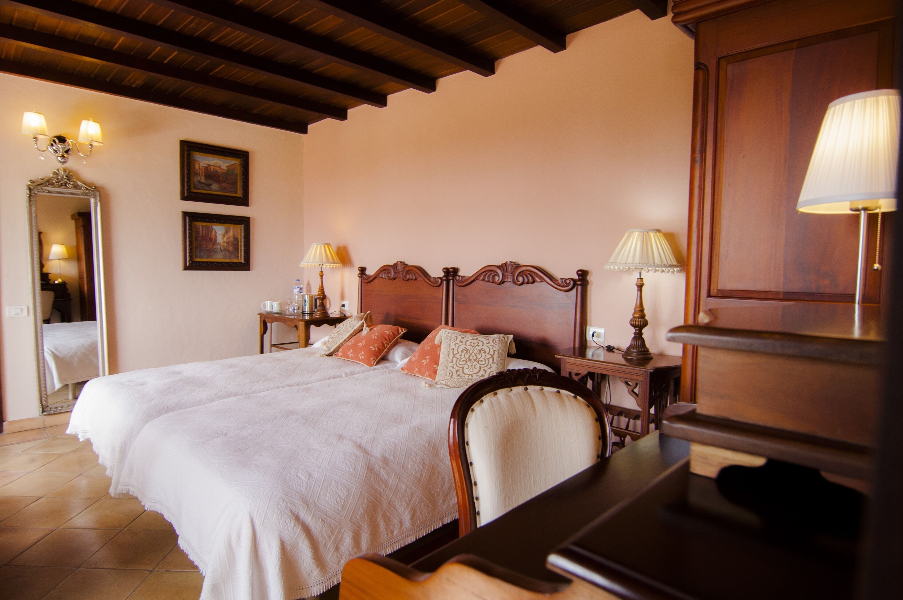 A neatly made bed with a wooden headboard, two bedside tables with lamps, a mirror, and two framed pictures on the wall.