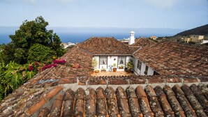 A traditional house with a tiled roof, surrounded by lush greenery and a view of the sea. - Finca Arminda (Villa de Mazo)