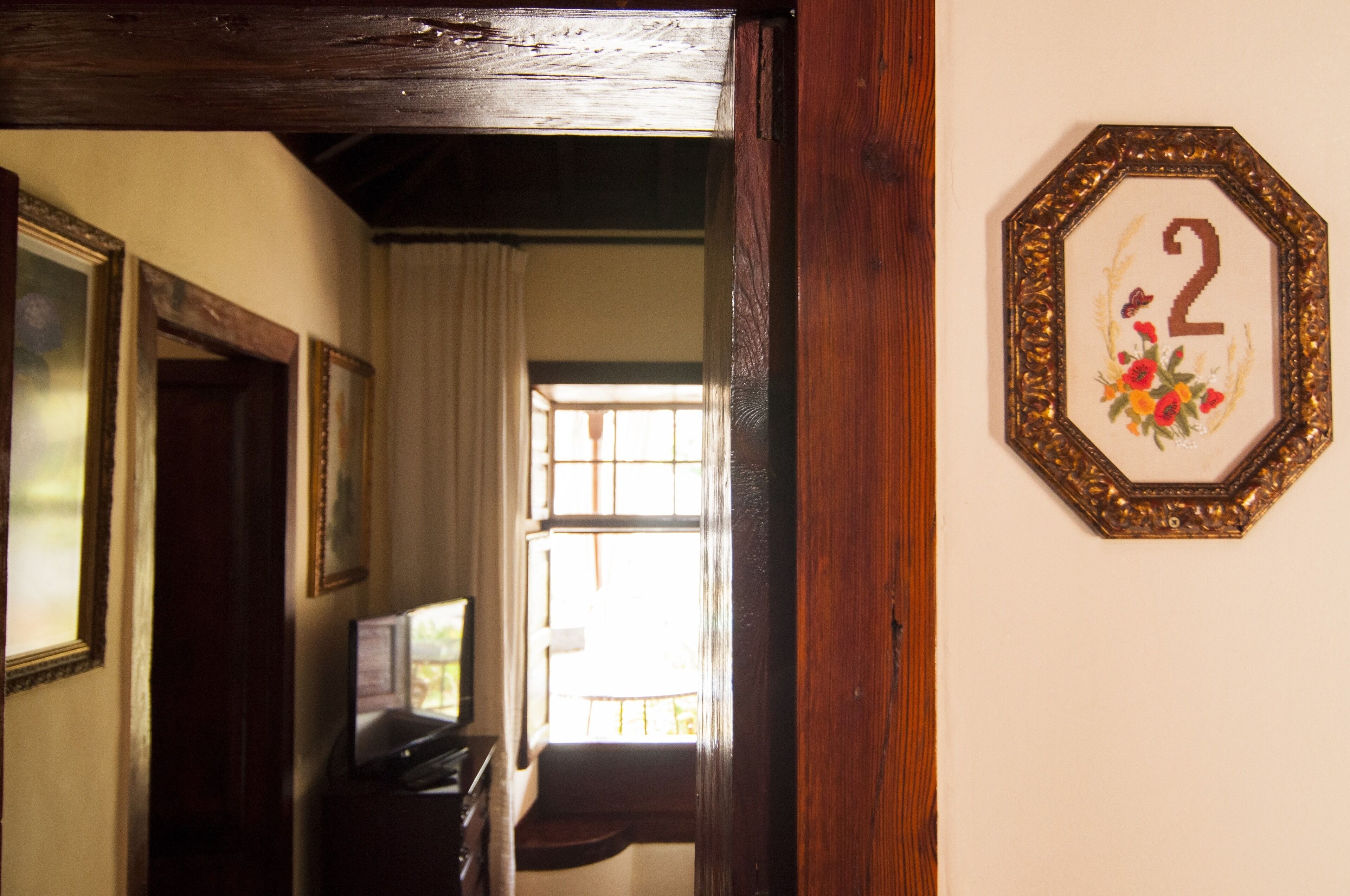 Un pasillo con un marco de puerta de madera, un número '2' enmarcado en la pared y una ventana con cortinas.