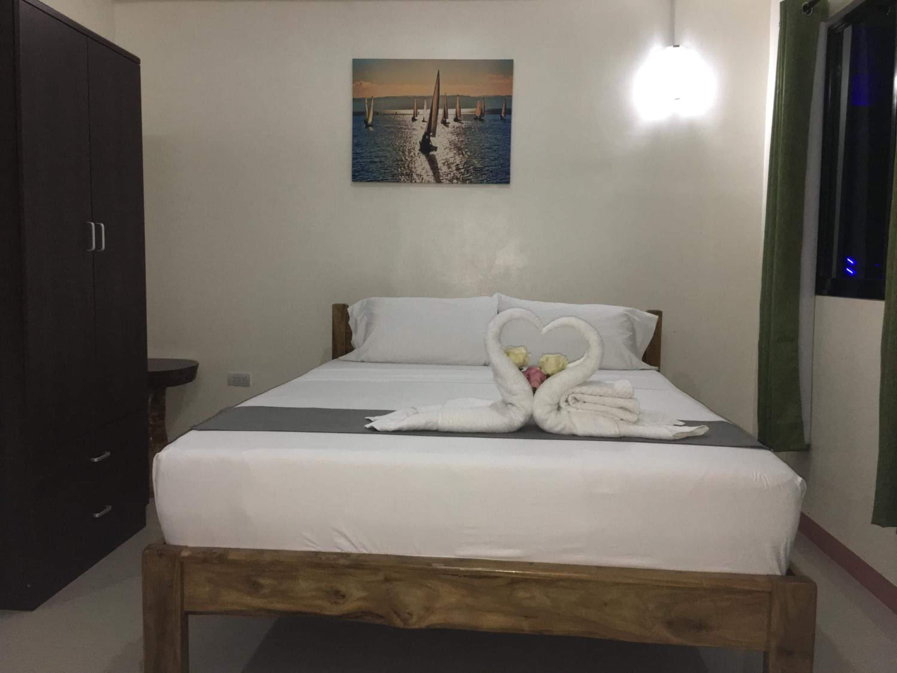 Una habitación de hotel con una cama, un cuadro de veleros en la pared y una decoración de toallas con forma de cisne.