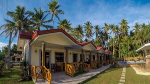 A row of single-story buildings with red roofs, surrounded by palm trees and a well-maintained lawn. - Aloha Seaside  Resort (San Juan)