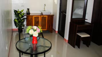 A room with a glass table, a red vase with flowers, a wooden cabinet, a television, and a plant.