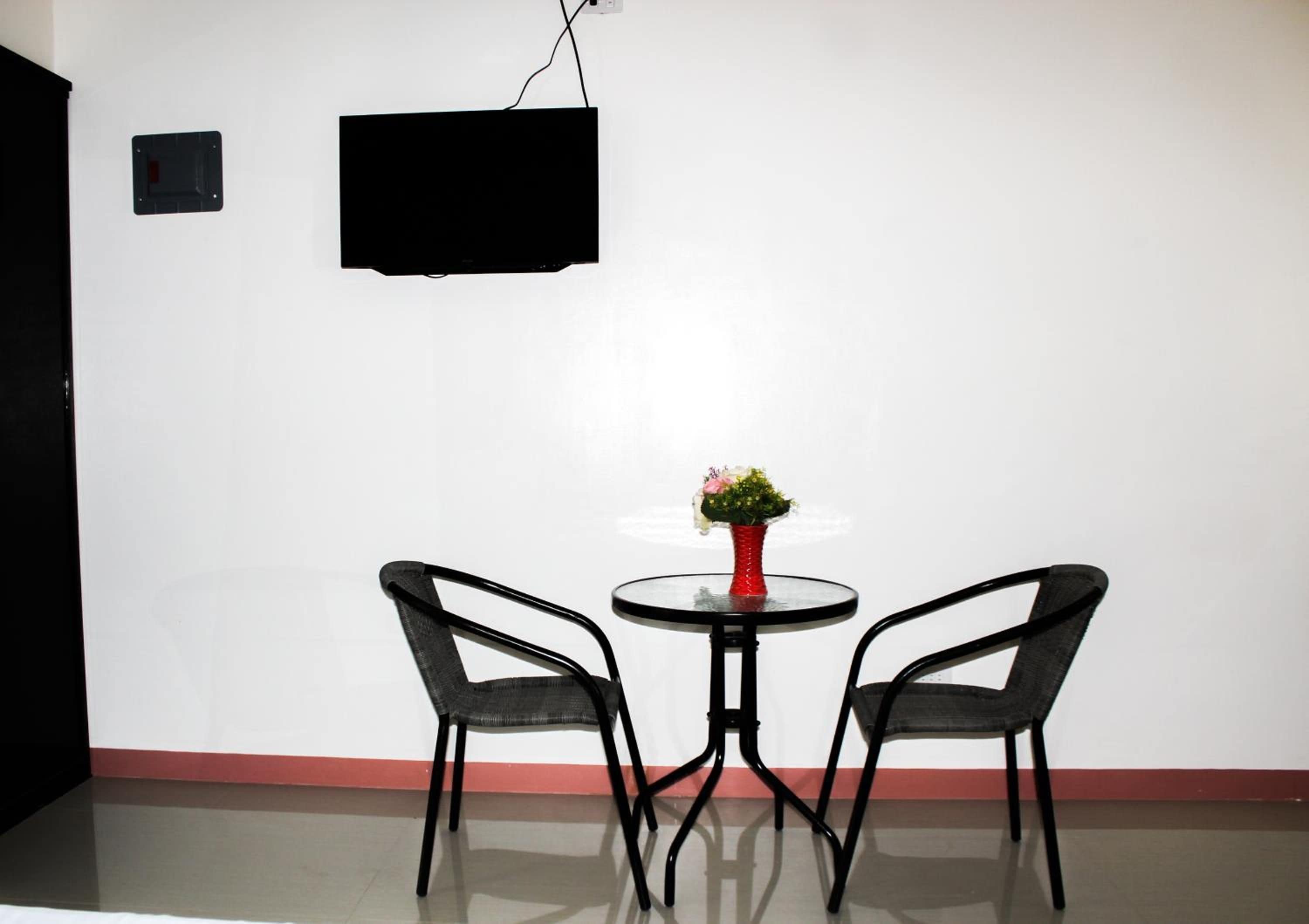 Une pièce comprenant deux chaises, une petite table ronde et un téléviseur fixé au mur.