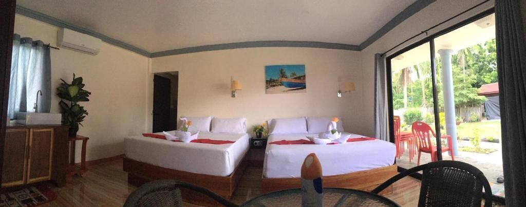 A hotel room with two beds, a dining table, a chair, a small table with a plant, and a view of the outdoors.