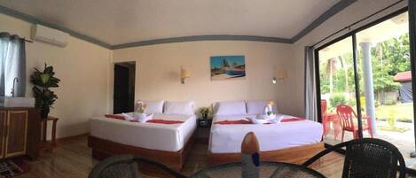 A hotel room with two beds, a dining table, a chair, a small table with a plant, and a view of the outdoors.