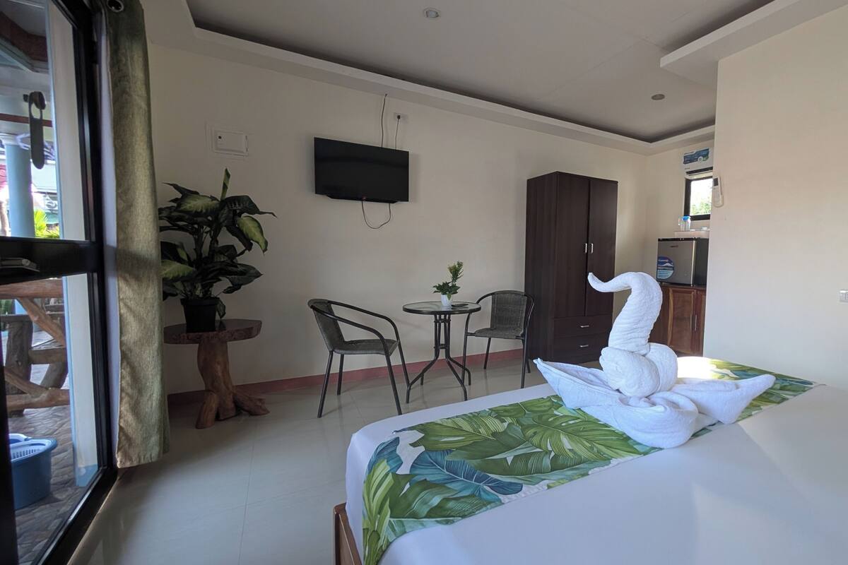 A hotel room with a bed, a TV mounted on the wall, a small table with chairs, and a wardrobe.