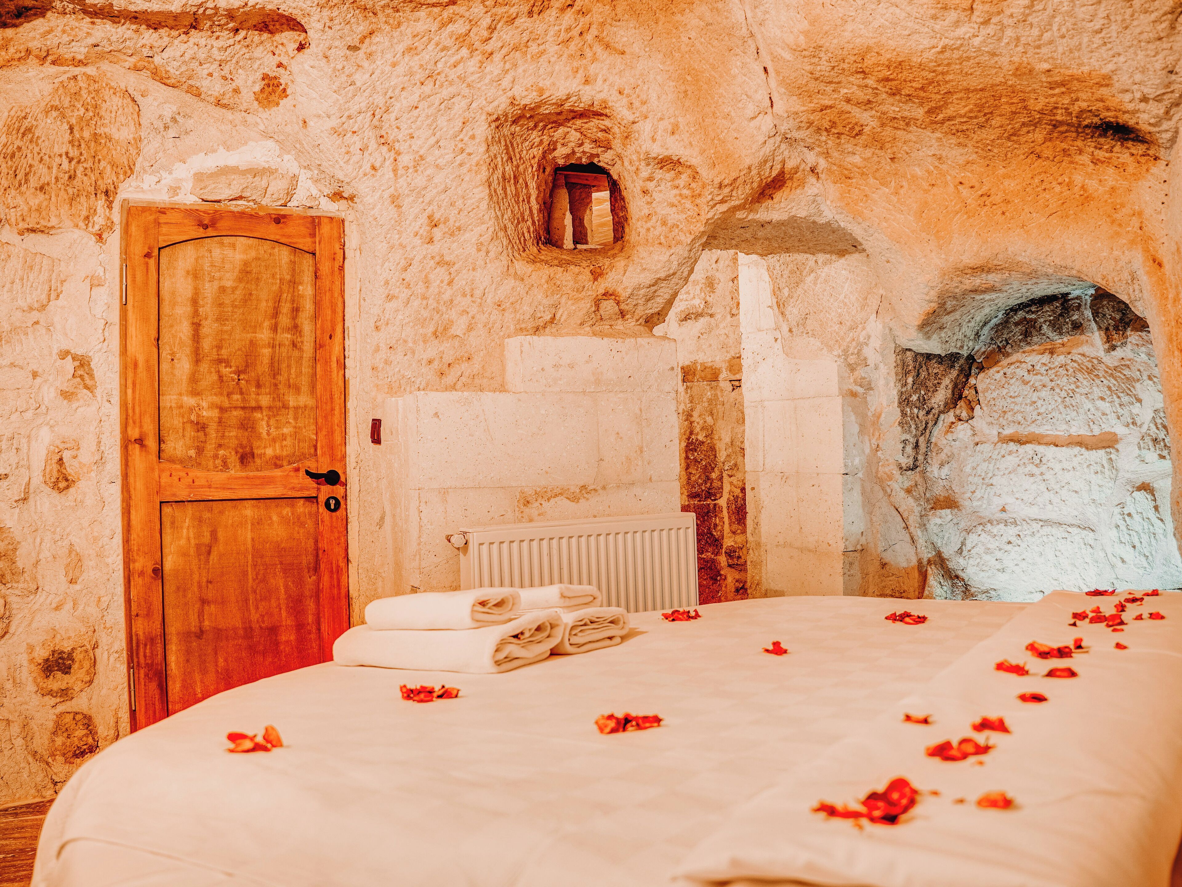 A rustic room with a wooden door, stone walls, a radiator, and a bed with rose petals.