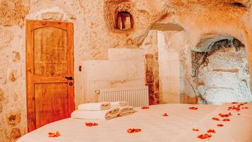 A rustic room with a wooden door, stone walls, a radiator, and a bed with rose petals.