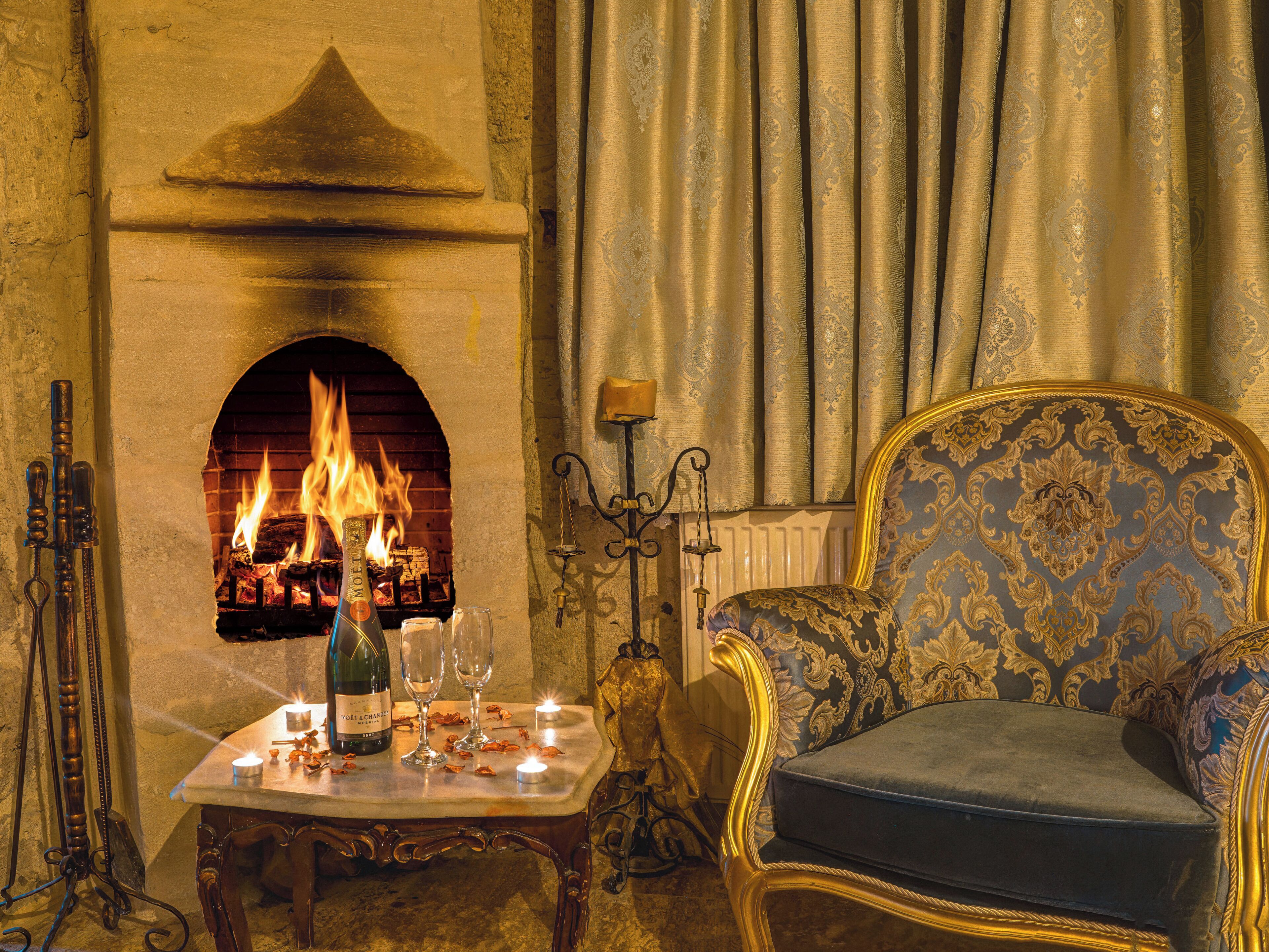 A room with a fireplace, a table with glasses and a bottle, and a patterned armchair.