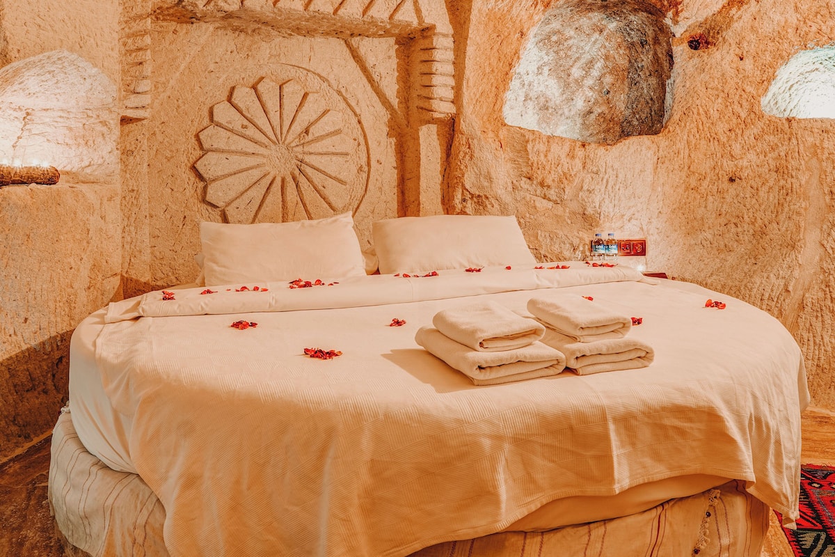 A bed with a white bedspread and pillows, a carved wall design, and a small bottle of water on the nightstand.
