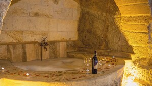 A stone bathtub with a bottle of wine and two glasses, surrounded by candles and rose petals. - Mahperi Cappadocia Cave (Nevsehir)