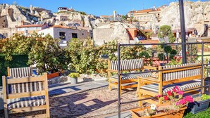 A rooftop terrace with wooden furniture and potted plants, overlooking a hillside with traditional buildings. - Mahperi Cappadocia Cave (Nevsehir)