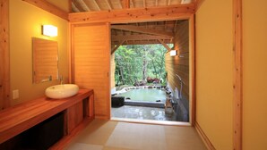 A wooden interior with a wooden bench, a sink, and a view of an outdoor hot spring area. - Tora no Yu (Kokonoe)