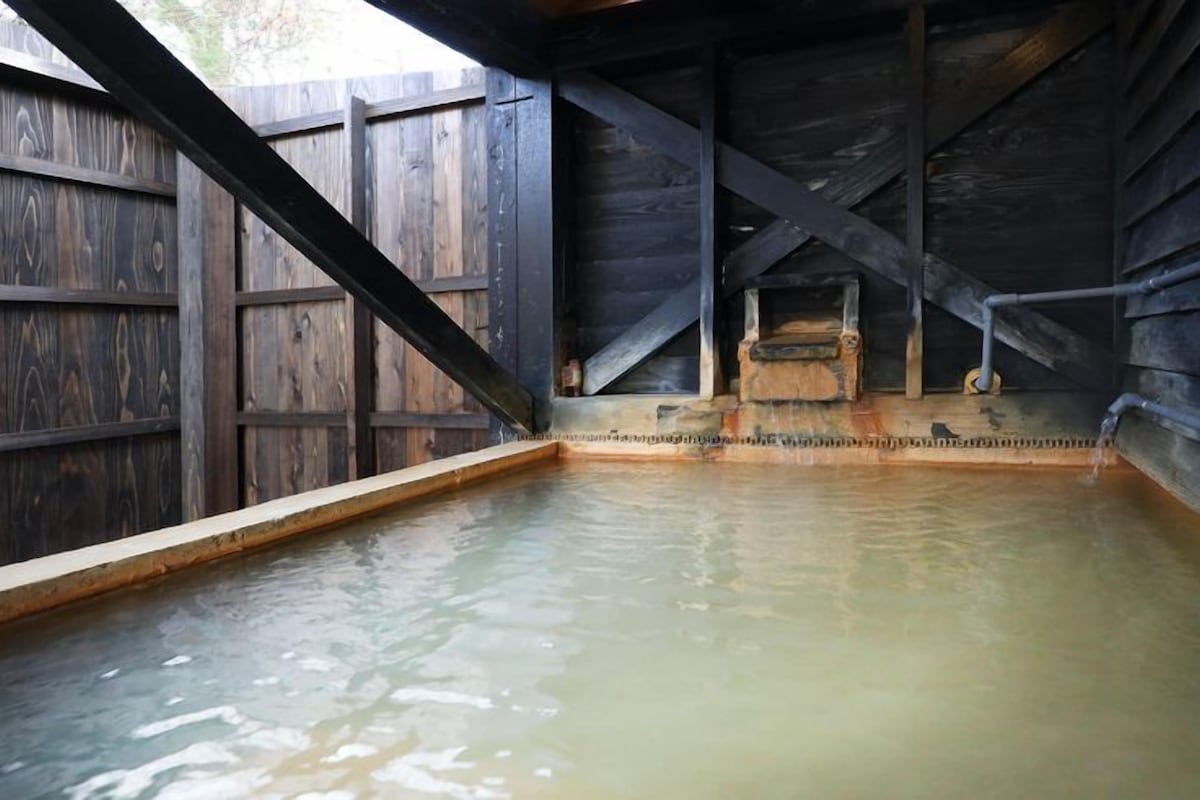 A wooden hot tub with a stone surround, set in a rustic wooden structure.