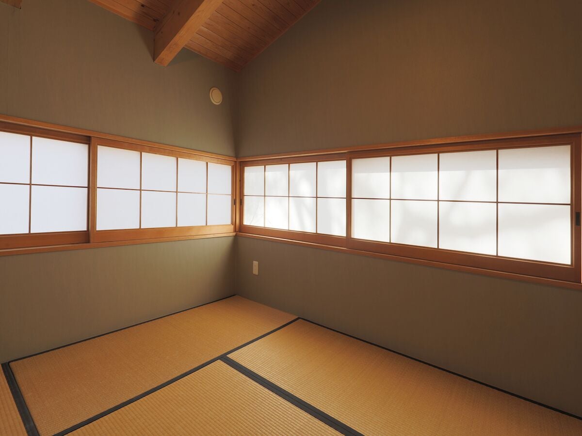 A traditional Japanese room with tatami flooring, shoji screens, and a wooden ceiling.