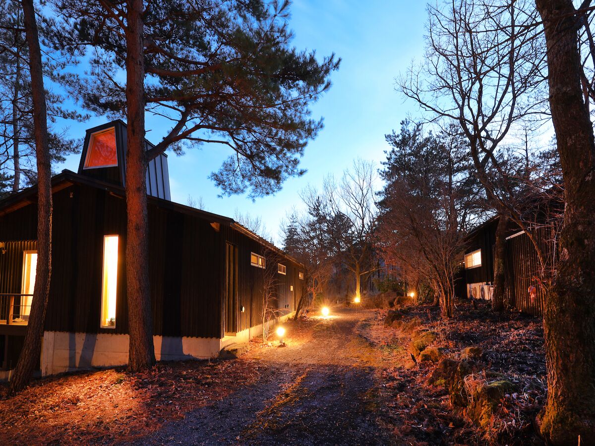 Un chalet rustique, accessible par un sentier de terre, et entouré d’arbres.