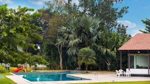 Una piscina rodeada de exuberante vegetación, un pabellón y un parque infantil.