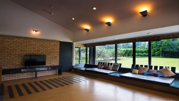 Amplia sala de estar con pared de ladrillo, televisor de pantalla plana, ventanas grandes y zona de estar con cojines.