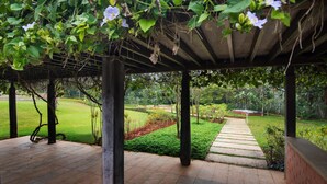 Un espacio al aire libre cubierto con una pérgola, suelo de piedra y un sendero que lleva a un campo de césped.
