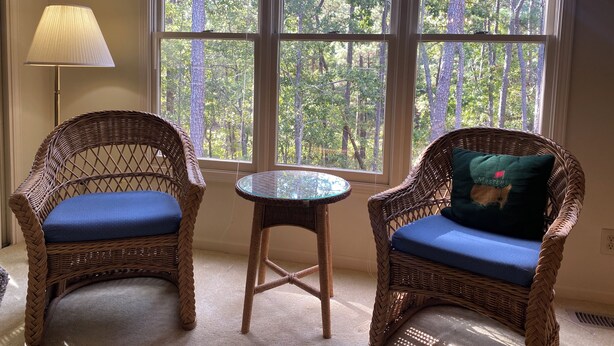 Een kamer met twee rieten stoelen met blauwe kussens, een glazen bijzettafeltje en een vloerlamp.