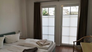Habitación de hotel con dos camas, una silla y vistas a través de un ventanal corredero.