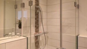 Un baño moderno con ducha acristalada, tocador con cubierta de vidrio y un espejo grande.