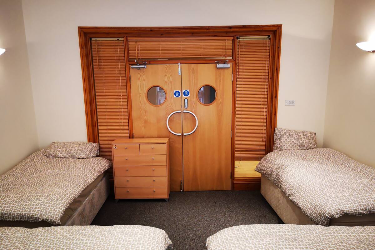A bedroom with two single beds, a wooden wardrobe with a mirror, and a small dresser.