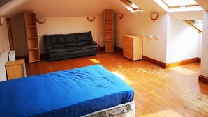 Quarto com área de dormir em mezzanine, sofá de couro preto, armário de madeira e claraboia.