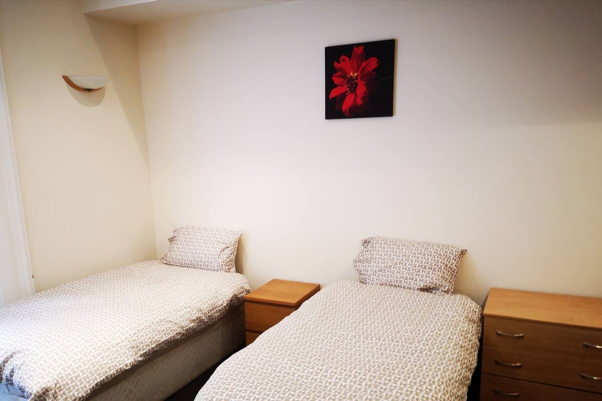 A bedroom with two single beds, a small bedside table, a wall-mounted light, and a framed picture.
